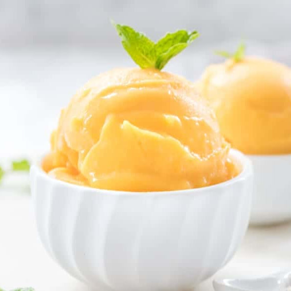 Two bowls of mango sorbet with mint leaves on a light background